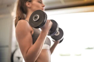 Focused woman lifting dumbbells in - Credits: pexels