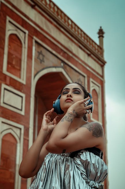 A tattooed woman wearing a tube top enjoys music with headphones outdoors in New Delhi. - Credits: pexels.com