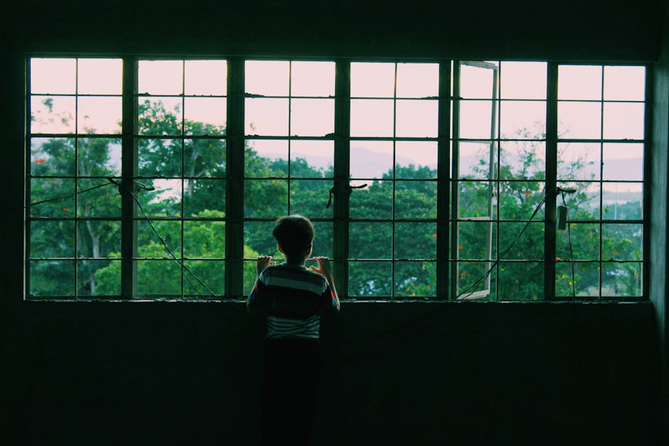 A young child looking through a large window with lush greenery outside. - Credits: pexels.com
