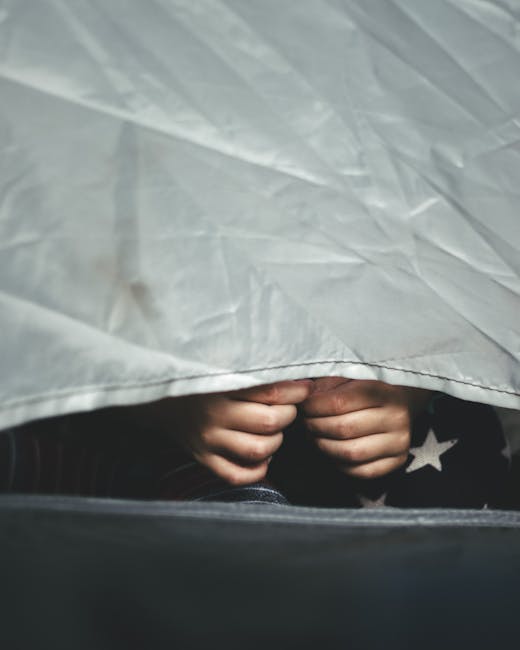 Close-up of child's hands peeking from under a gray fabric, conveying mystery. - Credits: pexels
